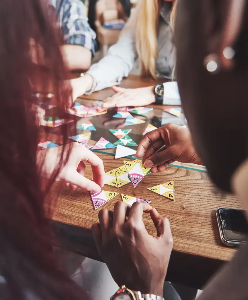 Mensen verzamelen zich rond een tafel en werken samen aan een kleurrijke puzzel met cijfers. De scène straalt teamwork en concentratie uit in een informele setting.
