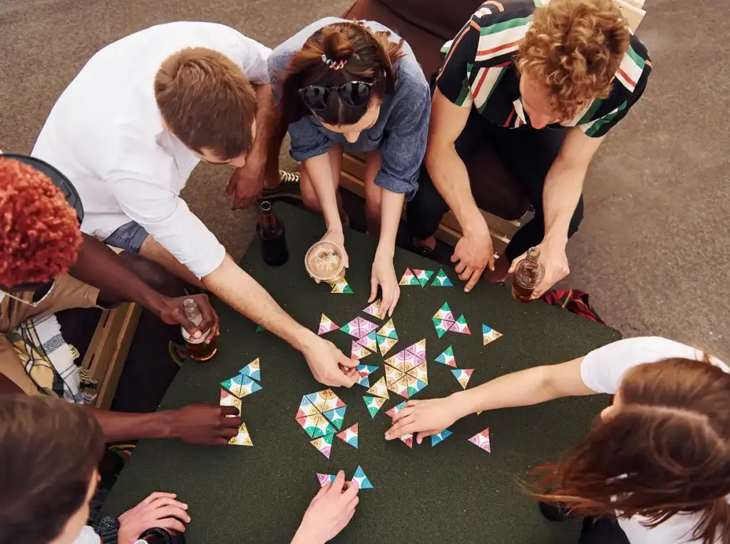 Bordspel met kleurrijke houten stukken op een groene kaart met tegels. Op de achtergrond rust een hand, wat een ontspannen, strategische sfeer uitstraalt.